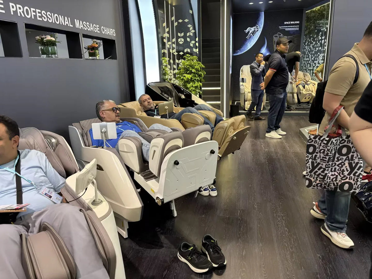 Men testing professional massage chairs at a trade show booth with modern decor.