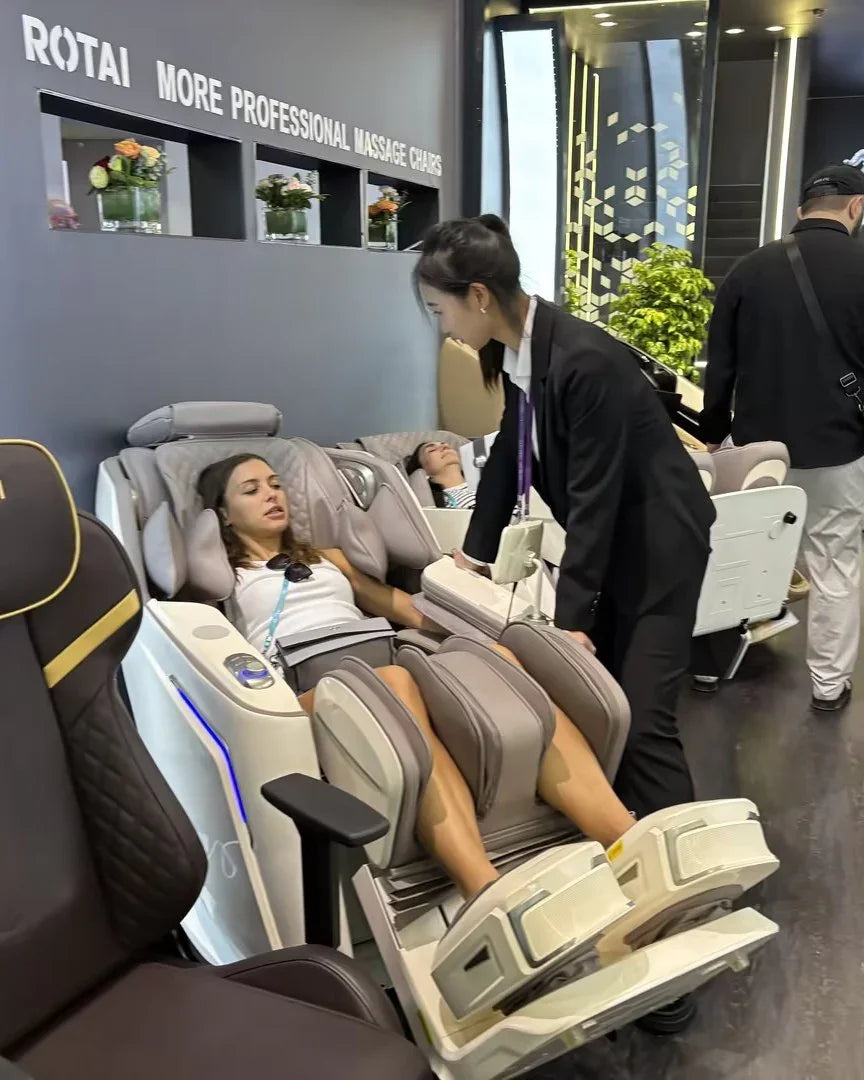 Woman relaxing in ROTAI massage chair at showroom, staff assisting, modern display area